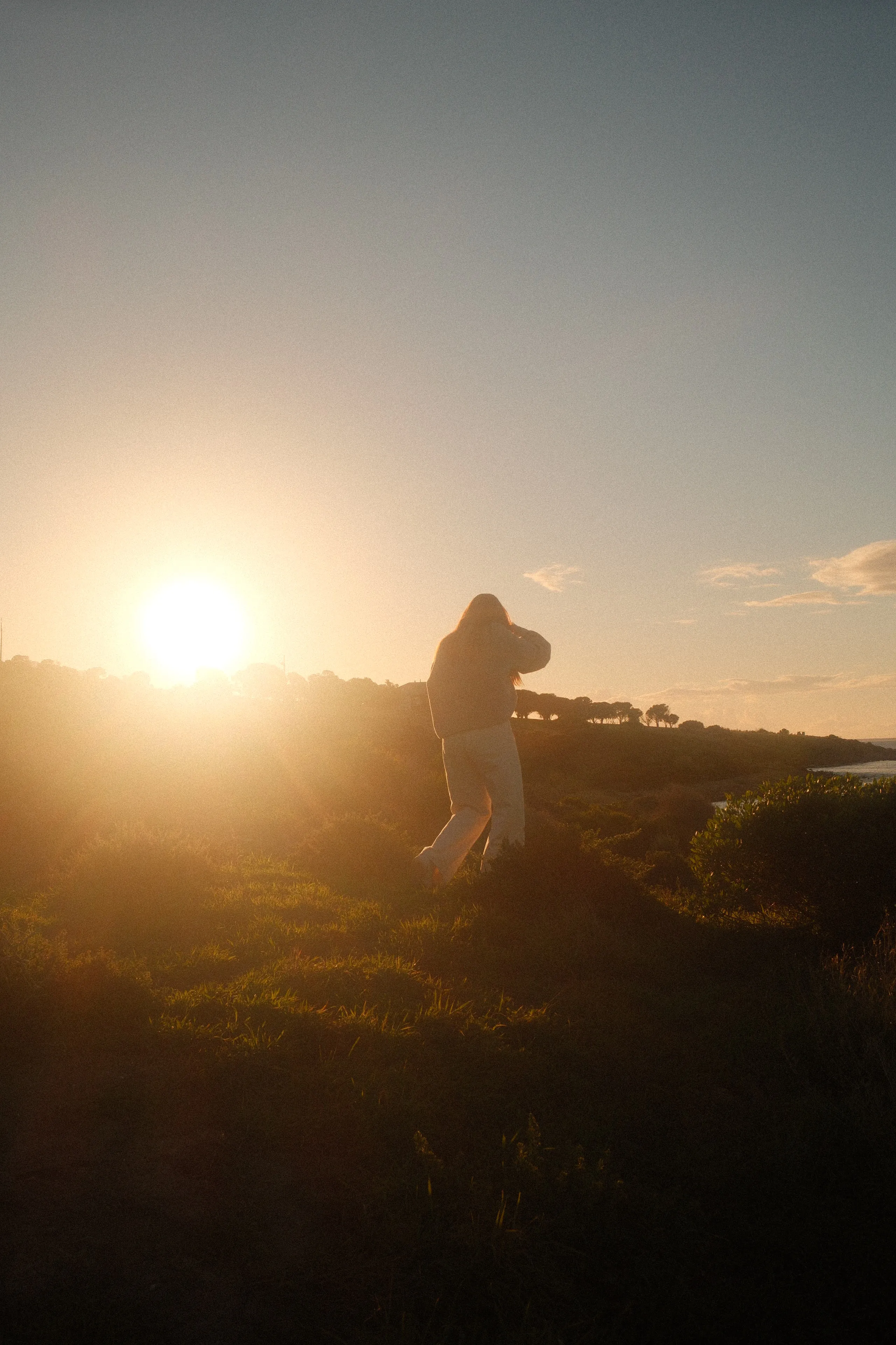 A figure in silhouette walking across a grassy headland into a low, glowing sun
