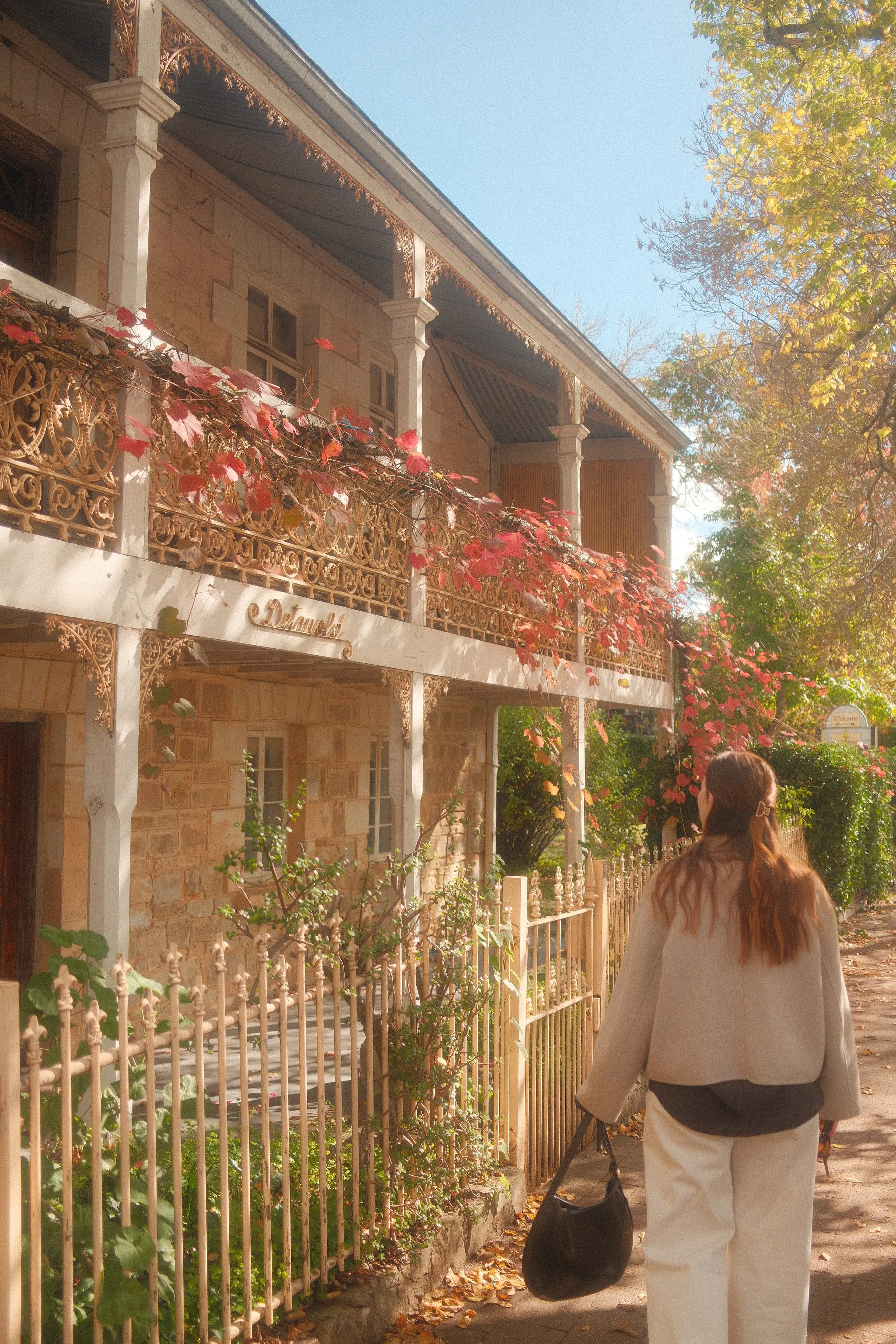 A woman walking past a sandstone terrace house with red autumn vines on its iron lace balcony
